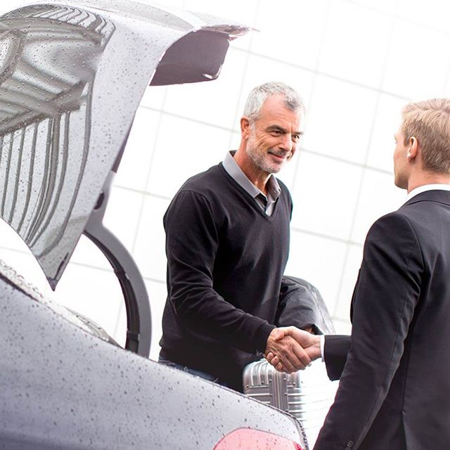 Ein Chauffeur gibt einem Fahrgast die Hand vor einer Limousine.