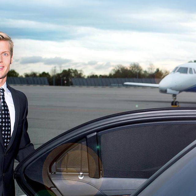 Ein Chauffeur öffnet die Tür einer Limousine, auf dem Rollfeld vor einem Business-Jet.